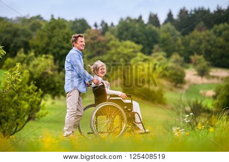 Senior man pushing woman sitting in wheelchair oustide in green autumn nature
