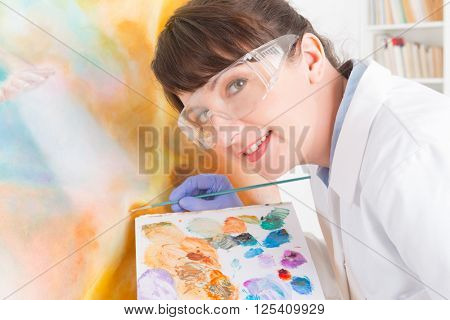 Artwork conservator at work with old painting wearing protective suit