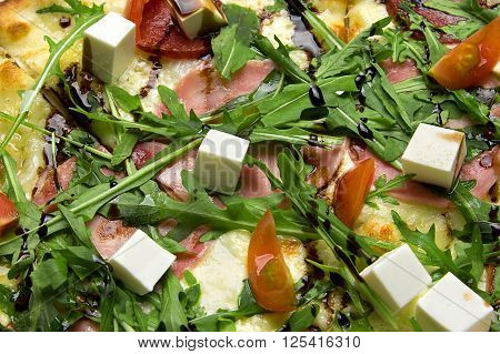 Appetizing pizza with ham, salami, arugula, cherry tomatoes, fetaksa, balsamic closeup