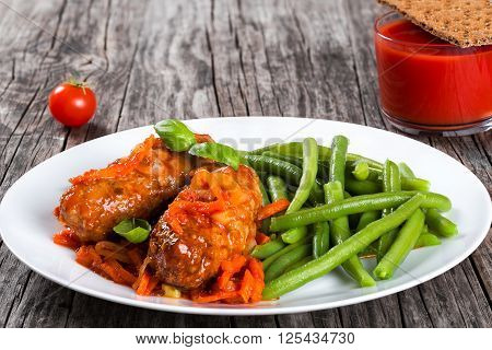 Delicious Meat Cutlets stewed with onion carrot tomato sauce decorated with basil leaves on a white dish with boiled green bean glass with tomato juice and wholegrain crispbread on the background close up top view