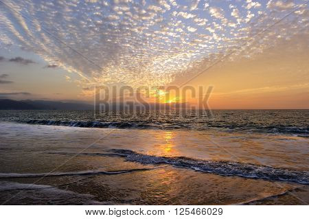 Ocean Sunset beach waves is an images of a rush of waves captured by a time exposure with a glowing red sunset cloud filled sky on the ocean horizon.