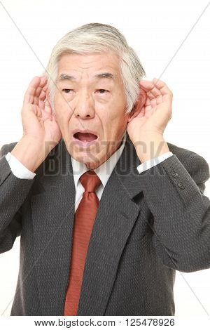 senior Japanese businessman with hand behind ear listening closely