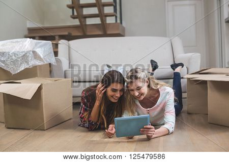 Friends lying together on the floor and using digital tablet in their new house