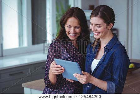 Two beautiful women using digital tablet in kitchen at home