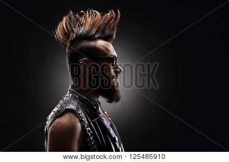 Profile shot of a young punk rocker with a Mohawk hairstyle on dark background