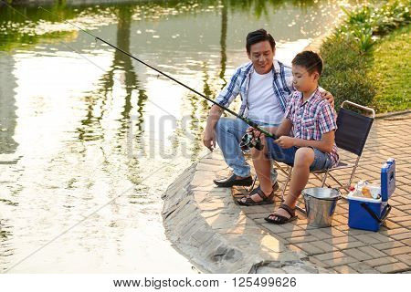 Proud father teaching his son fishing in tha park