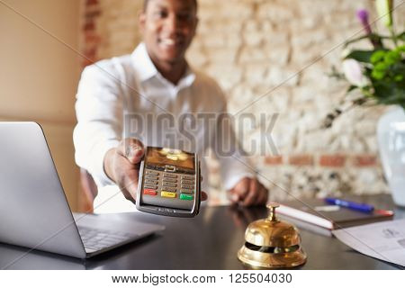 Concierge at hotel reception holds credit card reader to camera