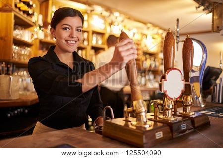 A young woman working behind a bar looking to camera, horizontal