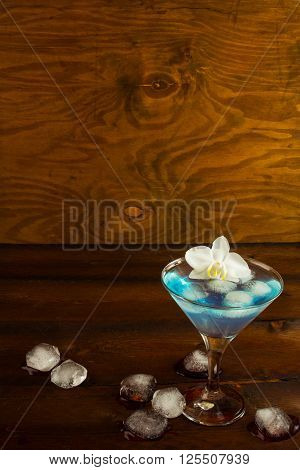 Blue cocktail in a martini glass with white orchid vertical copy space. Blue Martini. Blue curacao liqueur. Blue margarita. Blue Hawaiian cocktail