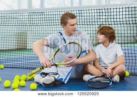 Resting young man or tennis coach with boy sitting near net.