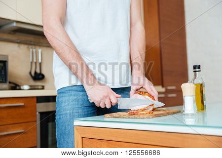 Closeup of young man stnding and cutting smoked meat on the kitchen 