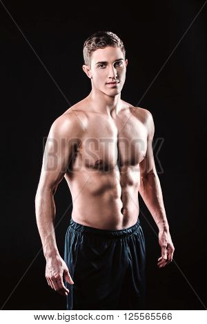 Attractive and muscular athlete. Studio shot of young shirtless sportsman on black background. Man looking at camera
