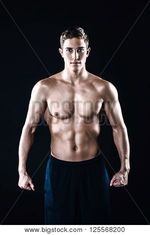 Attractive and muscular athlete. Studio shot of young shirtless sportsman on black background. Man looking at camera