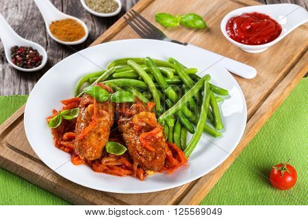 Delicious Meat Cutlets stewed with onion carrot tomato sauce decorated with basil leaves on a white dish with boiled green bean on a table napkin with fork top view