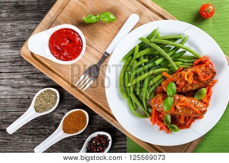 Delicious Meat Cutlets stewed with onion carrot tomato sauce decorated with basil leaves on a white dish with boiled green bean fork on a cutting board and spices on an old rustic table top view