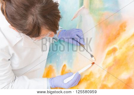 Artwork conservator at work with old painting wearing protective suit