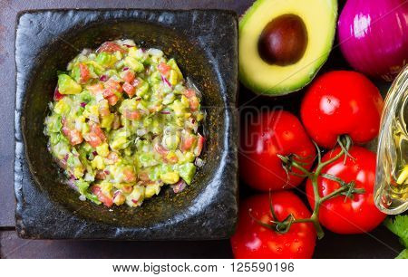 Guacamole - latin american mexican sauce in stone mortar and ingredients on dark background. Top view