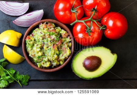 Guacamole - latin american mexican sauce in stone mortar and ingredients on dark background. Top view