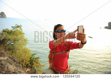 young woman hiker use smartphone taking photo on sunset seaside