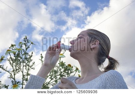 Young woman using inhaler to treat asthma allergic at flowers meadow
