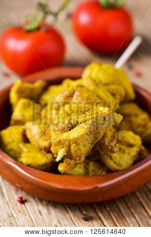 closeup of an earthenware bowl with some meat skewers on a rustic wooden table