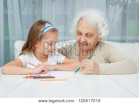 portrait of little girl with grandmother drawing with pencils