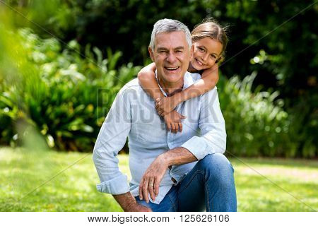 Happy grandfather and grandaughter smiling at yard