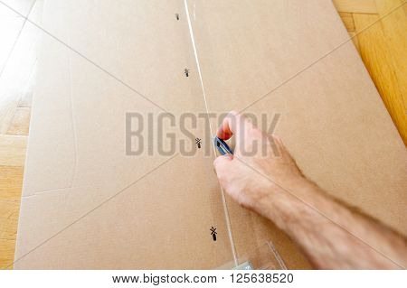 Caucasian man cutting a cardboard box with sharp steel box cutter knife while installing new furniture