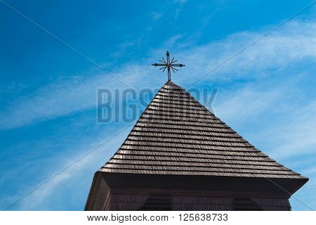 Dark brown roof made of wooden shingle with a cross on the top. Cloudy sky. Svaty Jur Slovakia Europe.