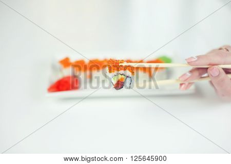 close up of chopsticks taking portion of sushi roll on the table restaurant / eating sushi roll using chopsticks