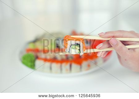 close up of chopsticks taking portion of sushi roll on the table restaurant / eating sushi roll using chopsticks