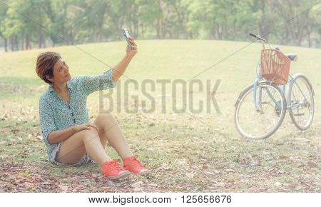 Selfie Young beautiful woman photographing themselves on a cell phone while sitting in prak with filter effect retro vintage style
