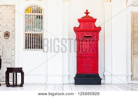 red and vintage postbox in front of an old building with stool