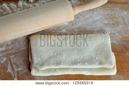 Folded Raw Puff Pastry Dough; Shown from above on a wooden cutting board lightly dusted with white flour. Wood rolling pin is also visible - above view.