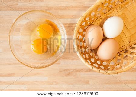 Eggs in braided bucket and raw eggs in glass pialat on light wooden background. Cusine background.