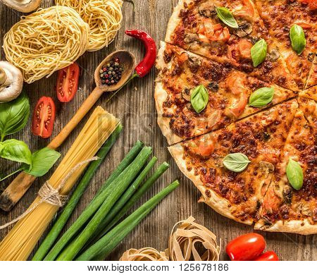 Italian food background with pizza, raw pasta and vegetables on wooden table