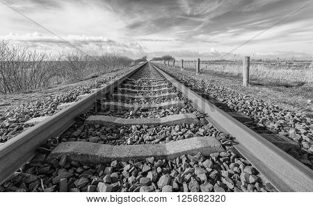Long straight railroad from rusty rails on concrete sleepers in a rural area in the Netherlands.