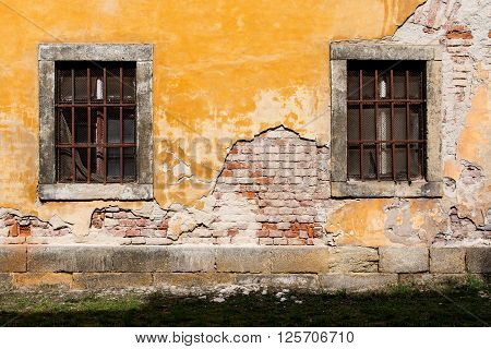 old damaged yellow plastered brick wall with barred windows and a lawn