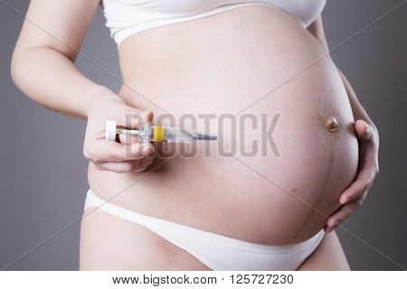 Young pregnant woman making injection in the stomach. Close-up studio shot on a gray background