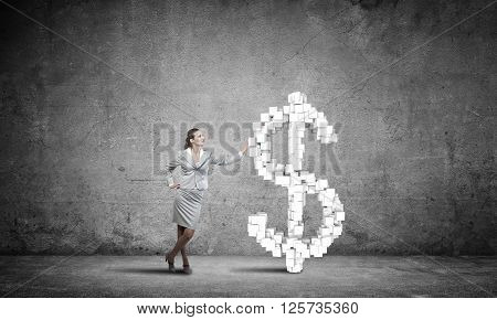 Young confident businesswoman leaning on big dollar sign