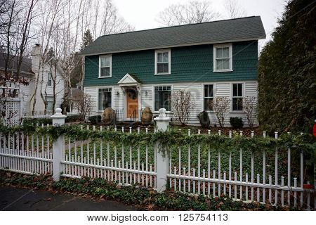 HARBOR SPRINGS, MICHIGAN / UNITED STATES - DECEMBER 23, 2015: A white metal picket fence, decorated with a Christmas garland, in front of a home in Harbor Springs.
