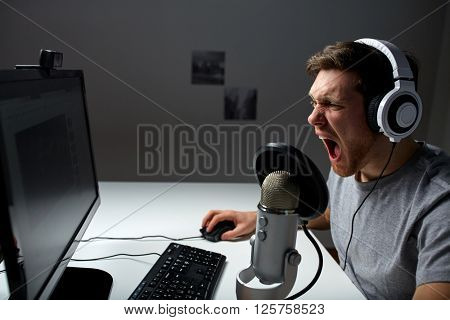 technology, gaming, entertainment, let's play and people concept - angry screaming young man in headset with pc computer playing game at home and streaming playthrough or walkthrough video