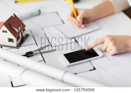 business, architecture, building, construction and people concept - close up of architect hand with living house blueprint and smarphone writing to notebook