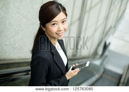 Business woman going down to escalator and hold with a cellphone
