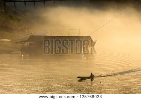 Misty tropical sunset on lake with boat and wooden home in Sangklaburi, Thailand