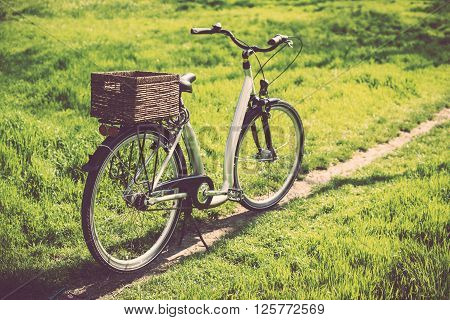 City bicycle with a wicker basket stands on a footpath in a park