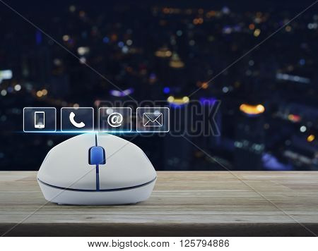 Wireless computer mouse with telephone mobile phone at and email buttons on wooden table in front of blurred light city tower Customer support concept