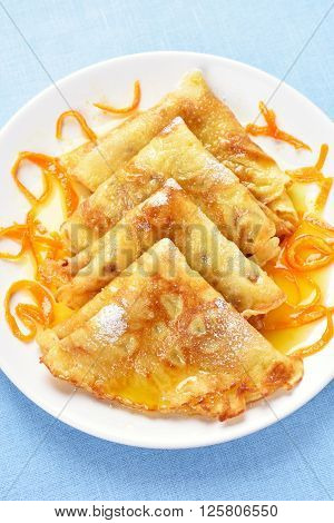 Crepes with orange syrup on white plate over blue background top view