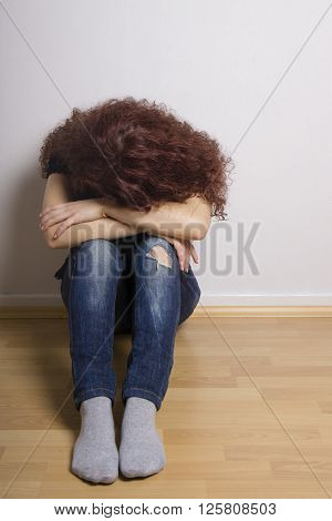 sad depressed young woman hiding her face sitting on floor