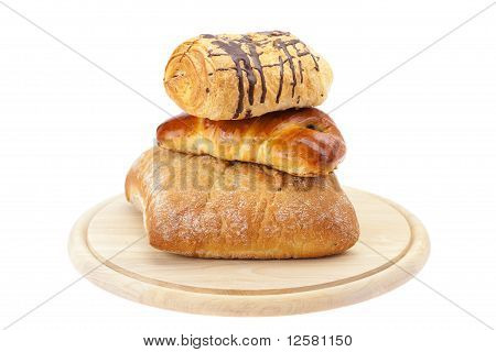 Pão, rolo com sementes de papoila e rolo com o Chocolate em uma placa de corte isolado no branco